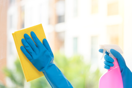 Hands of housekeeper cleaning mirror with yellow cloth.