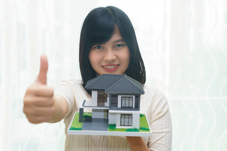 Happy young woman thumps up or like with house model on handsの写真素材