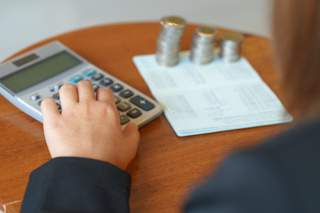 Hands of businesswoman pushing on calculator with account book and coins.の写真素材