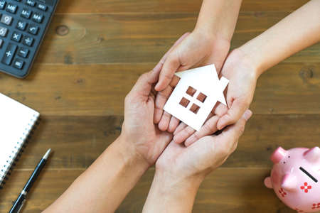 Top view of a couple hands holding house paper with calculator, notebook and piggy bankの写真素材