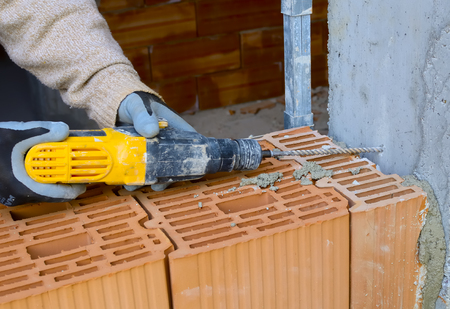 Mason drills a hole with a power drill on a column in of reinforced concrete