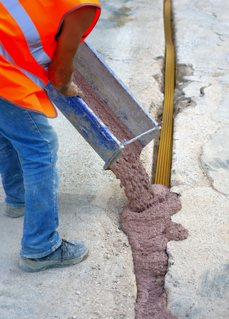 fiber optic cables buried in a micro trench with concrete colored red by a workerの写真素材