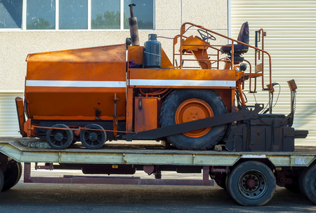 A paver finisher, asphalt finisher or paving machine waiting to be transported on a road being asphaltedの写真素材