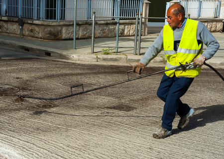 Road worker spraying bitumen emulsion with the hand spray lance before applying a new layer of asphaltの写真素材