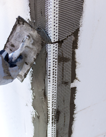 Construction site - Installing external insulation. Facade thermal insulation works with stopping and surfacer.
Selective focus and motion blur on tool.の写真素材