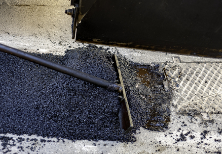 worker leveling fresh asphalt during asphalt pavement repair or construction works