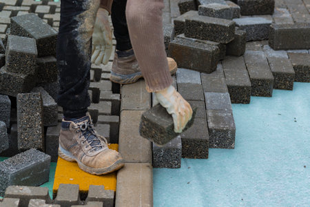 Construction worker laying interlocking paving concrete onto sheet nonwoven bedding sand and fitting...