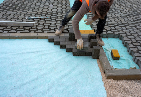 Construction worker laying interlocking paving concrete onto sheet nonwoven bedding sand and fitting them into place.の写真素材