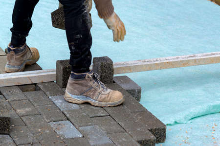 Construction worker laying interlocking paving concrete onto sheet nonwoven bedding sand and fitting them into place.の写真素材