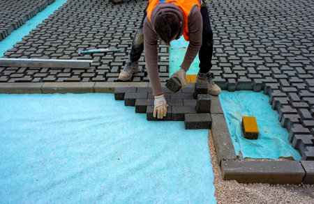 Construction worker laying interlocking paving concrete onto sheet nonwoven bedding sand and fitting them into place.の写真素材