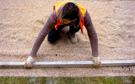 Construction worker laying interlocking paving concrete onto sheet nonwoven bedding sand and fitting them into place.の写真素材