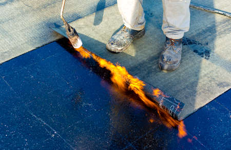 Worker preparing part of bitumen roofing felt roll for melting by gas heater torch flameの写真素材