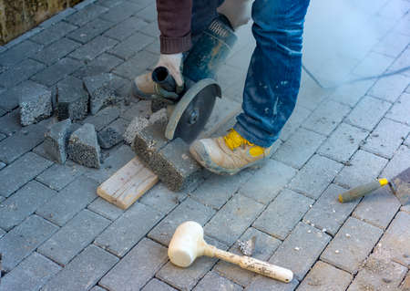 Worker cuts a tile to size with an electric grinder to complete the self-locking pavingの写真素材
