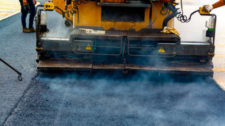 Workers regulate tracked paver laying asphalt heated to temperatures above 160Â° pavement on a runwayの写真素材