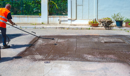 Road worker spraying bitumen emulsion with the hand spray lance before applying a new layer of asphaltの写真素材