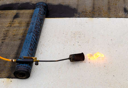Material and equipment for waterproofing roofs and terraces. Roll of bituminous sheath, propane torch and glove resting on a bituminous membrane already laid.の写真素材