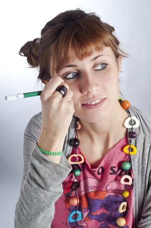 Young girl with pigtails, and colorful necklace laying and writes with a pen on her faceの写真素材