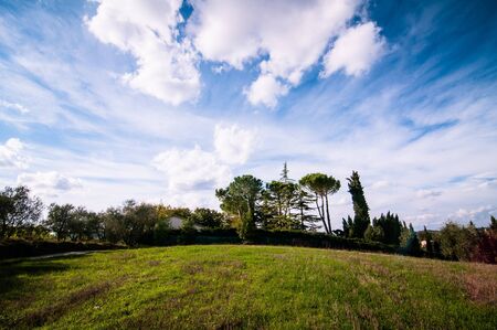 Tuscan countryside landscape with blue sky, clouds and meadowsの写真素材