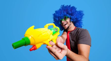 Funny guy with blue wig and water gun on blue backgroundの写真素材