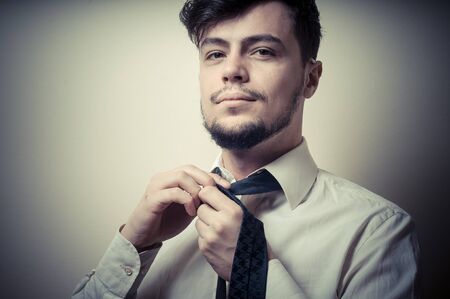 Sexy stylish businessman adjusting tie on gray backgroundの写真素材