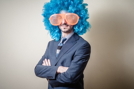 funny businessman with big orange glasses and blue wig on gray backgroundの写真素材