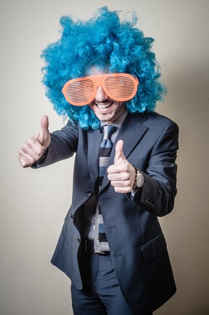funny businessman with big orange glasses and blue wig on gray backgroundの写真素材