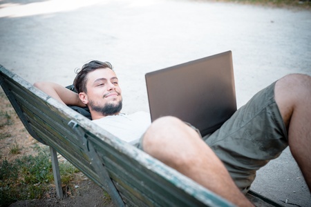 young stylish man using notebook at the park