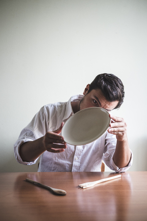 young stylish man with white shirt eating in mealtimes behind a tableの写真素材