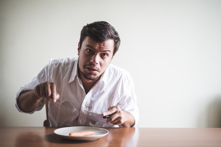 young stylish man with white shirt eating carrot behind a tableの写真素材