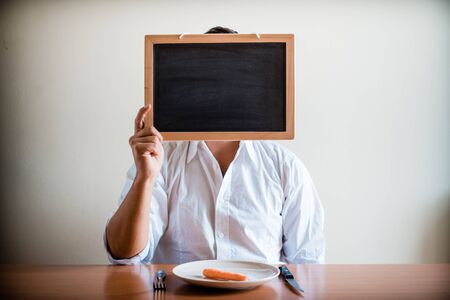young stylish man with white shirt holding blackboard behind a table