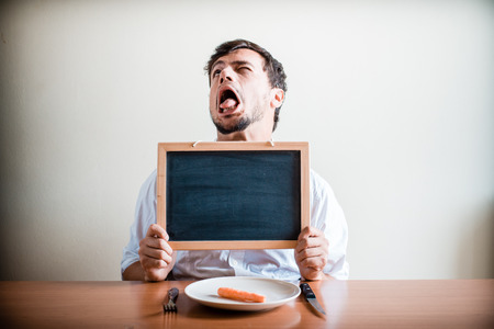young stylish man with white shirt holding blackboard behind a tableの写真素材