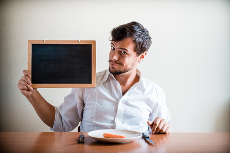 young stylish man with white shirt holding blackboard behind a tableの写真素材