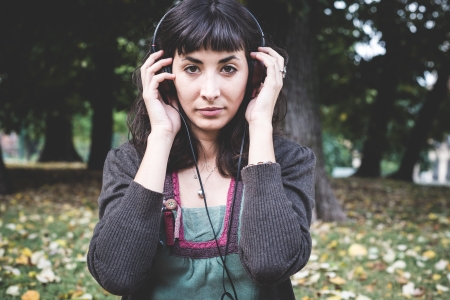 young beautiful woman listening to music at the park in autumnの写真素材