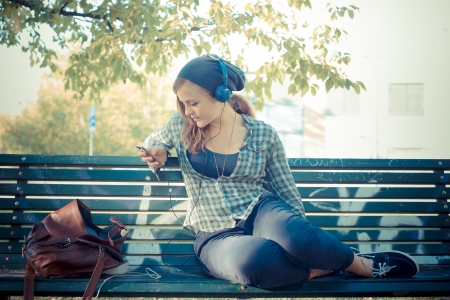 beautiful young blonde hipster woman listening music in the park on the benchの写真素材