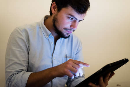 young man using and illuminated by the light of tablet at home の写真素材