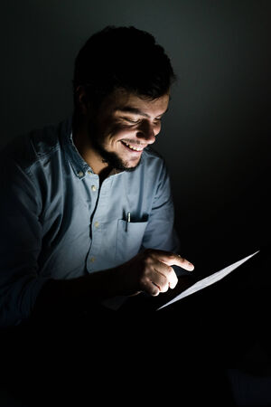 young man using and illuminated by the light of tablet at home の写真素材