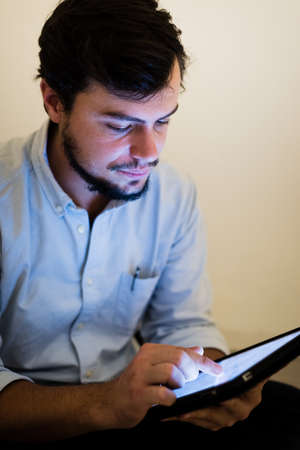 young man using and illuminated by the light of tablet at home の写真素材