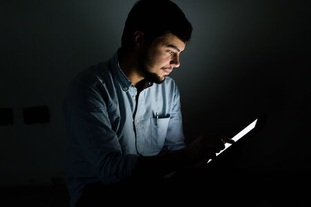 young man using and illuminated by the light of tablet at home の写真素材