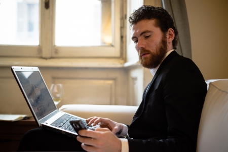 handsome bearded hipster elegant man using laptop and cellphoneの写真素材