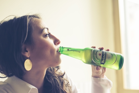 MILAN, ITALY - JANUARY 16, 2014: Woman drinking heineken beer glass bottle 33 cl. Heineken International is a Dutch brewing company, founded in 1864 in Amsterdam, famous all over the world.のeditorial素材