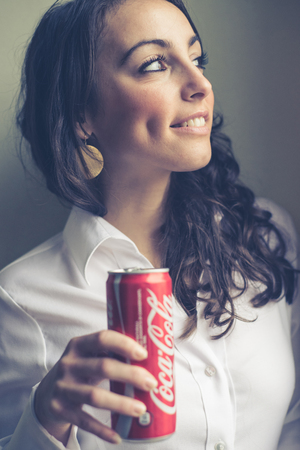 MILAN, ITALY - JANUARY 16, 2014: Beautiful woman drinking coca cola bottle can 33 cl. Coca Cola is the most famous brand soft drink in the worldのeditorial素材