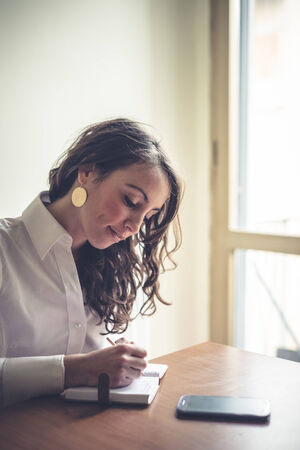 beautiful woman at home writing and working with diary and smart phone