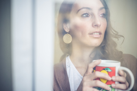 beautiful woman with cup facing through window at home 