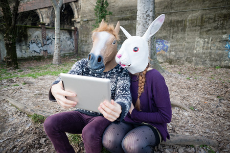 young hipster cuople horse and rabbit mask using tablet at the parkの写真素材