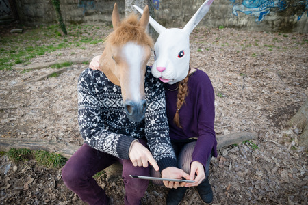 young hipster cuople horse and rabbit mask using tablet at the park