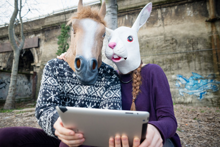young hipster cuople horse and rabbit mask using tablet at the parkのeditorial素材