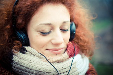 young beautiful red curly hair woman listning music at the parkの写真素材