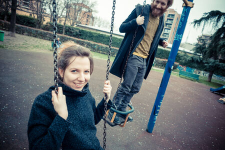 young modern stylish couple playing swings outdoors