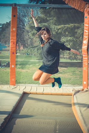 young beautiful blonde hipster woman jumping on trampoline outdoorsの写真素材