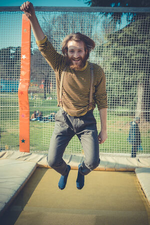 young bearded stylish handsome hipster man jumping on trampoline at playground 
